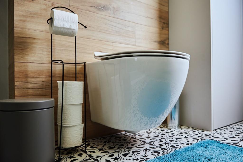 A remodeled bathroom with a modern toilet, wooden accent wall, tissue rack, and patterned floor tiles